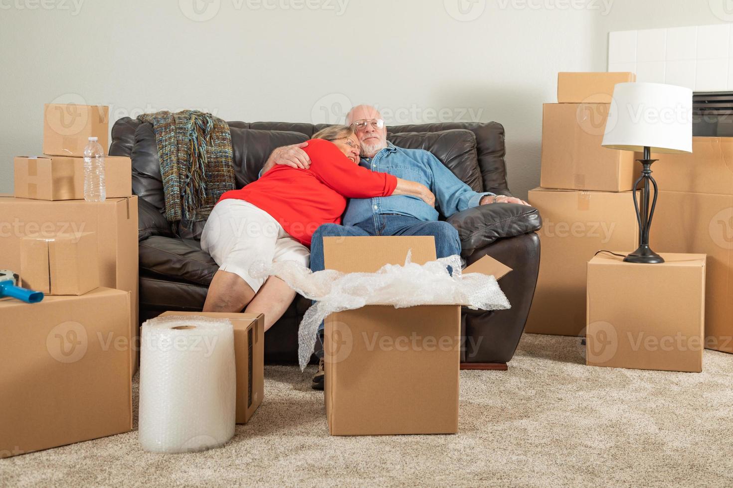 couple adulte fatigué et affectueux reposant sur un canapé entouré de cartons de déménagement photo