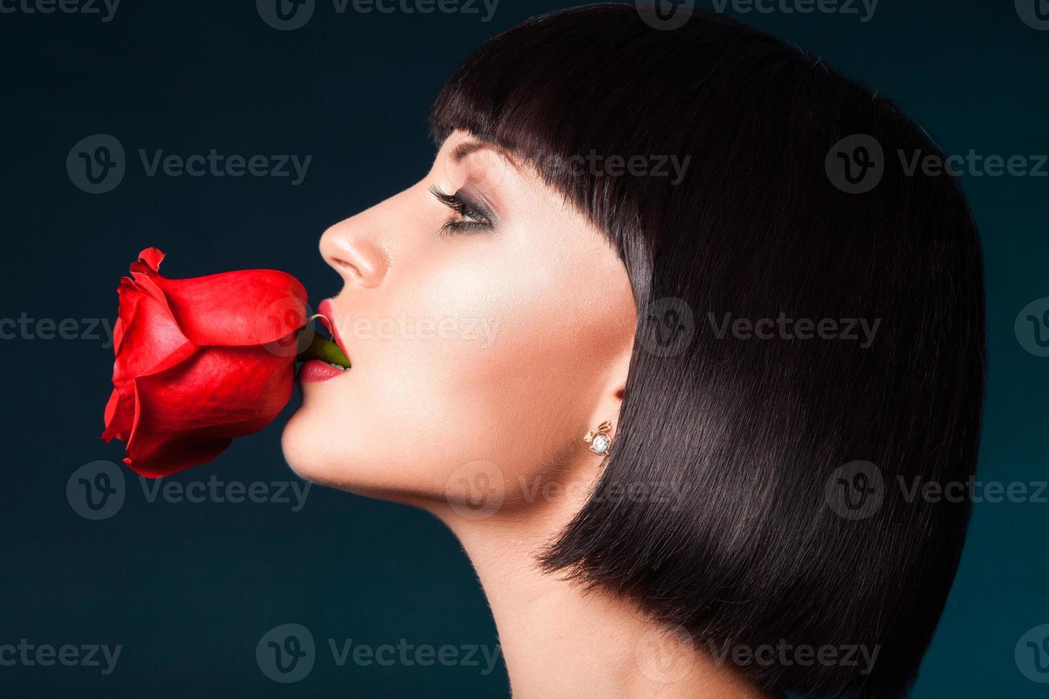 demi-visage portrait de jolie femme avec une rose rouge dans la bouche photo