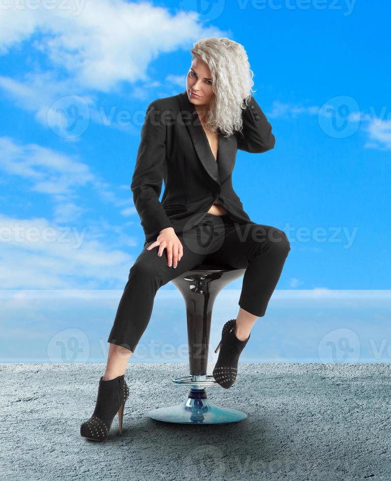 femme aux yeux bleus est assise sur une chaise en costume noir photo