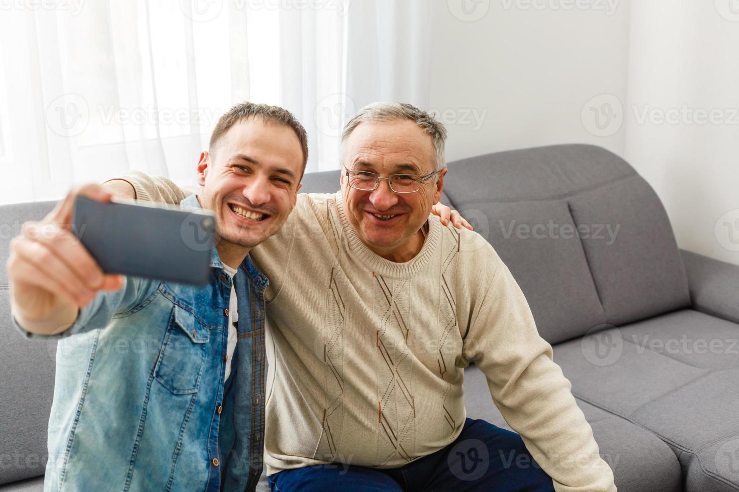 un fils adulte souriant s'assoit sur un canapé se détend avec un père âgé parle en partageant ses pensées en regardant dans les yeux, un homme heureux du millénaire se repose sur un canapé parle avec un père âgé profite d'un week-end de loisirs en famille à la maison. photo
