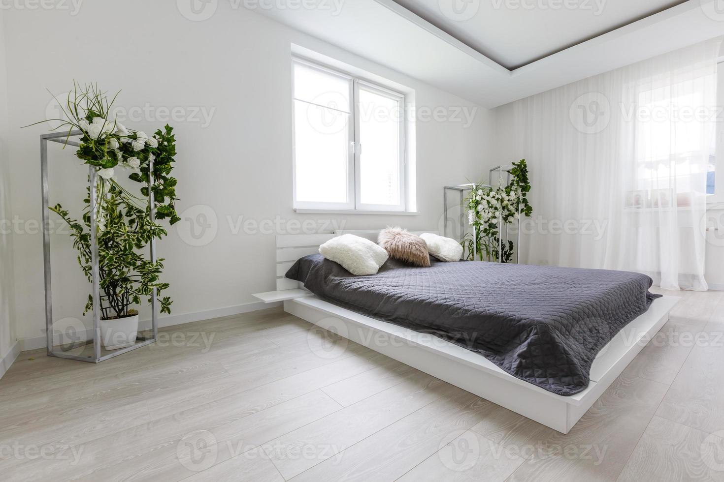 chambre lumineuse avec mur blanc, grand lit avec literie grise et meubles faits à la main photo