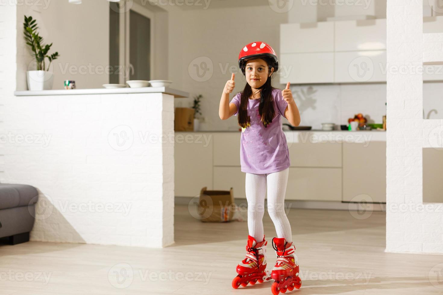 Petite fille aux cheveux bouclés avec des patins à roulettes en t-shirt rose et un chapeau souriant heureux photo