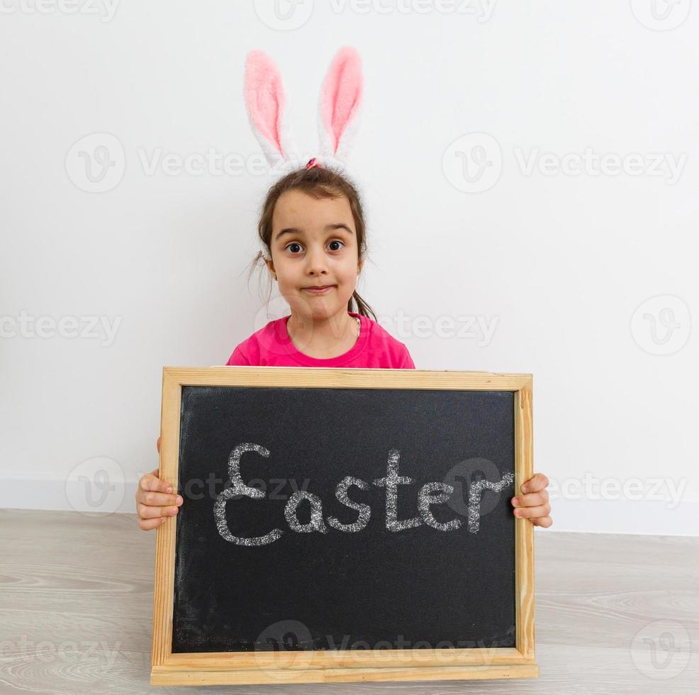 petite fille en costume de lapin blanc. l'enfant tient une feuille noire avec un espace pour le texte. photo