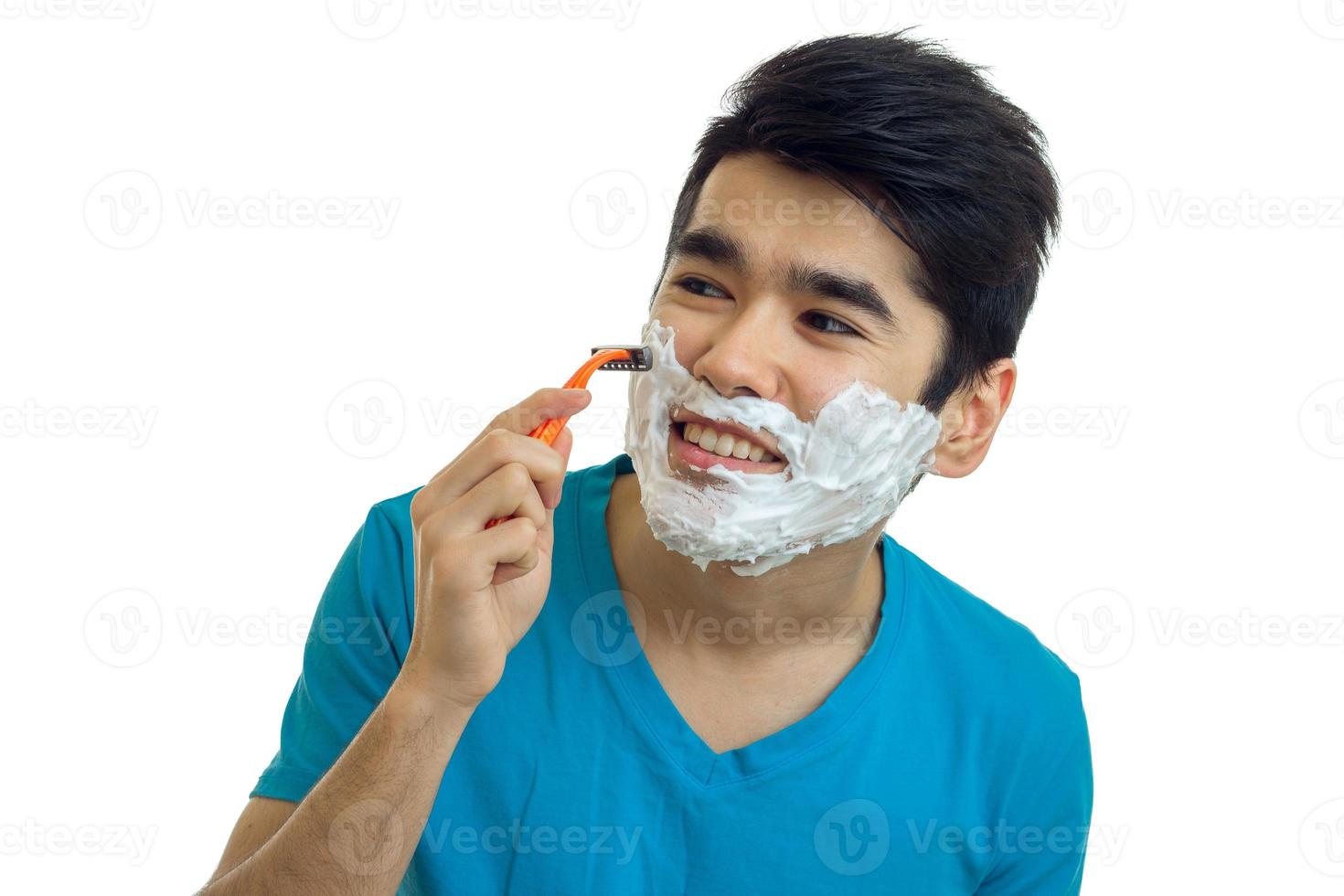 jeune homme avec de la mousse sur le visage regarde ailleurs en souriant et se rase la barbe en gros plan photo