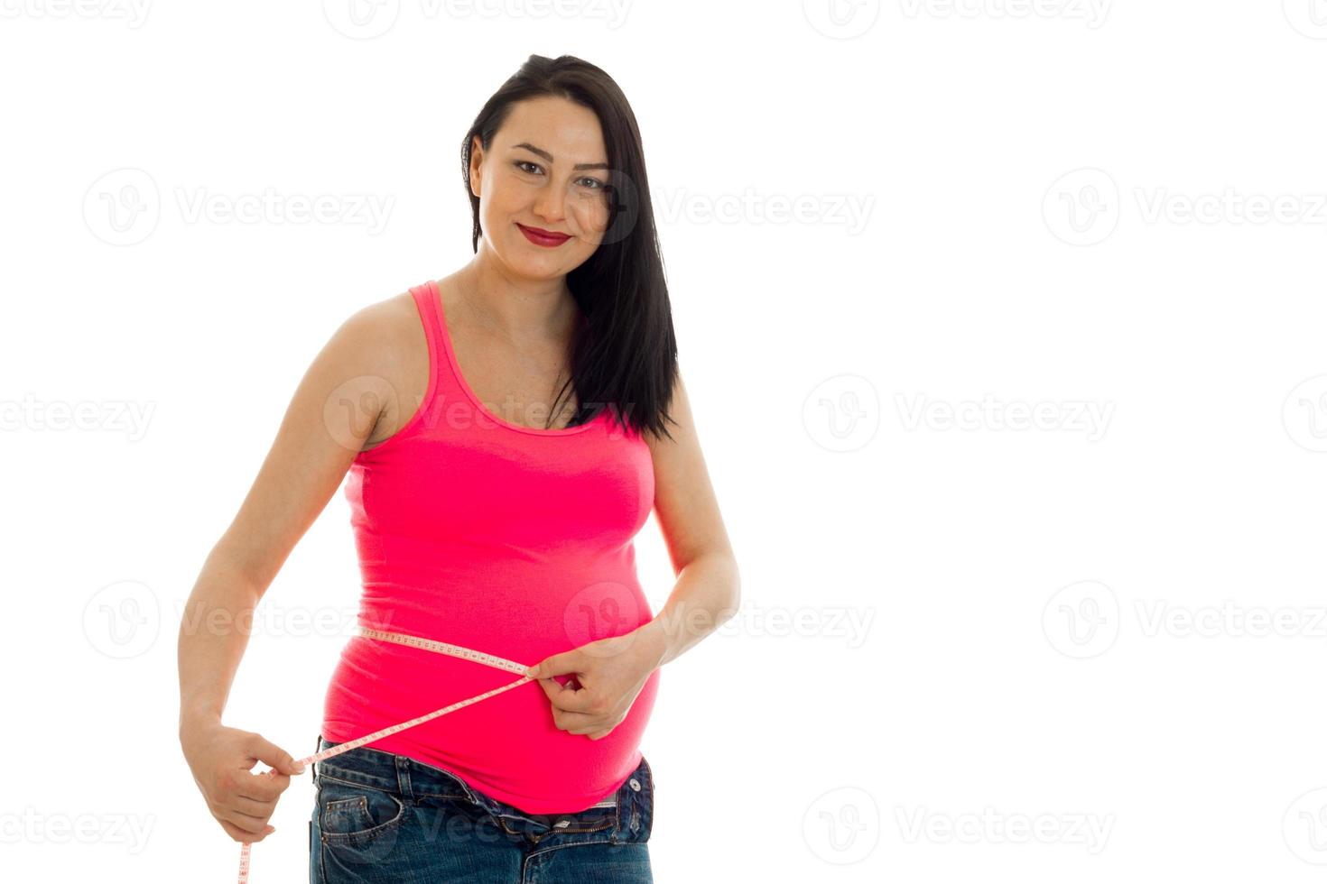 portrait de jeune jolie femme enceinte mesurer son ventre avec du ruban adhésif et souriant à la caméra isolé sur fond blanc photo