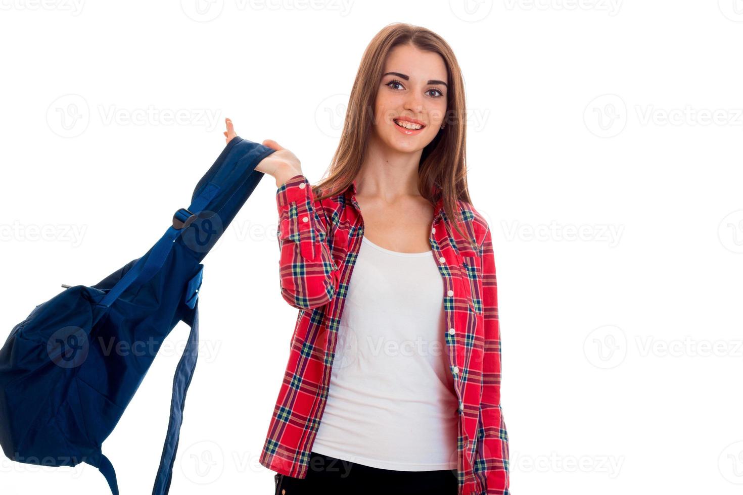 Belle jeune étudiante brune adolescente dans des vêtements élégants et sac à dos dans les mains posant isolé sur fond blanc photo