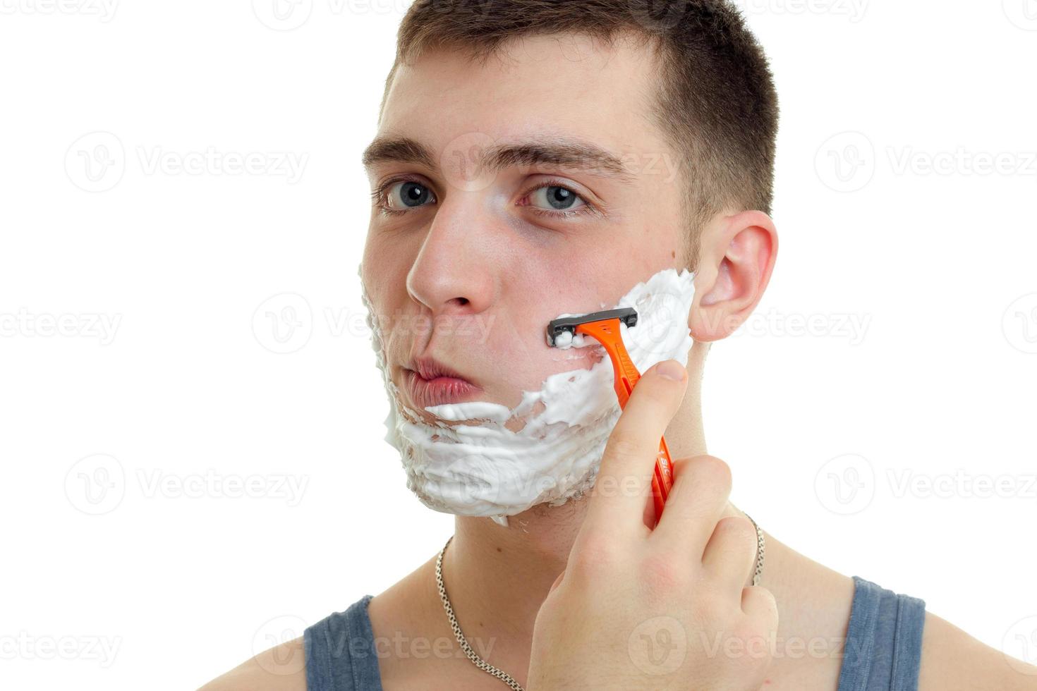 portrait d'un charmant jeune homme avec de la mousse sur le visage qui regarde bien et la machine rase la barbe photo