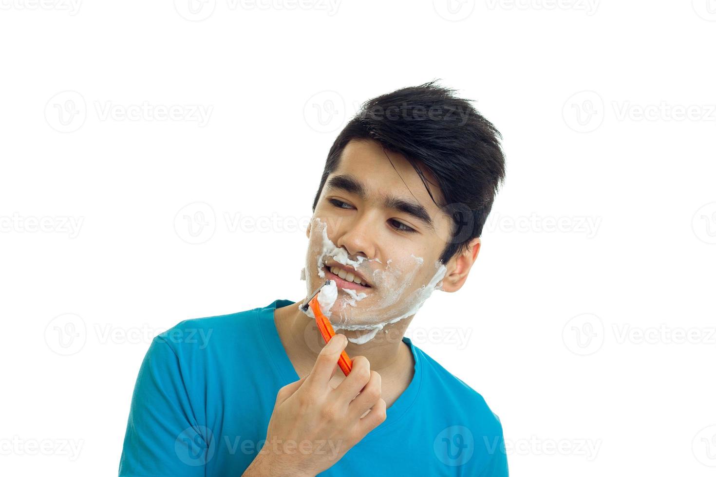 jeune homme souriant aux cheveux noirs se dresse avec de la mousse sur son visage en regardant de côté et en gros plan rasé photo