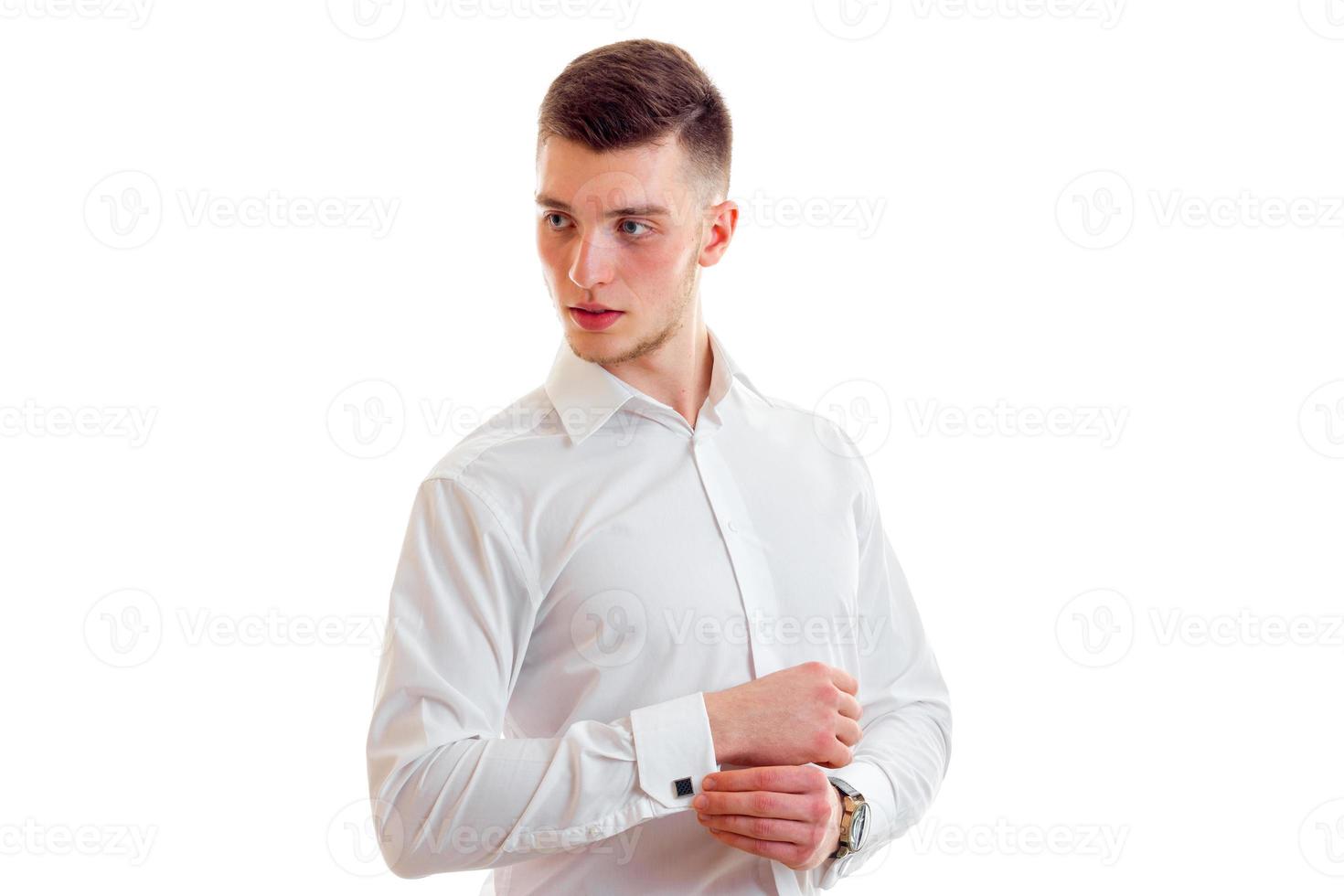 un jeune homme élégant dans une chemise blanche regarde ailleurs et s'ajuste par la manche photo