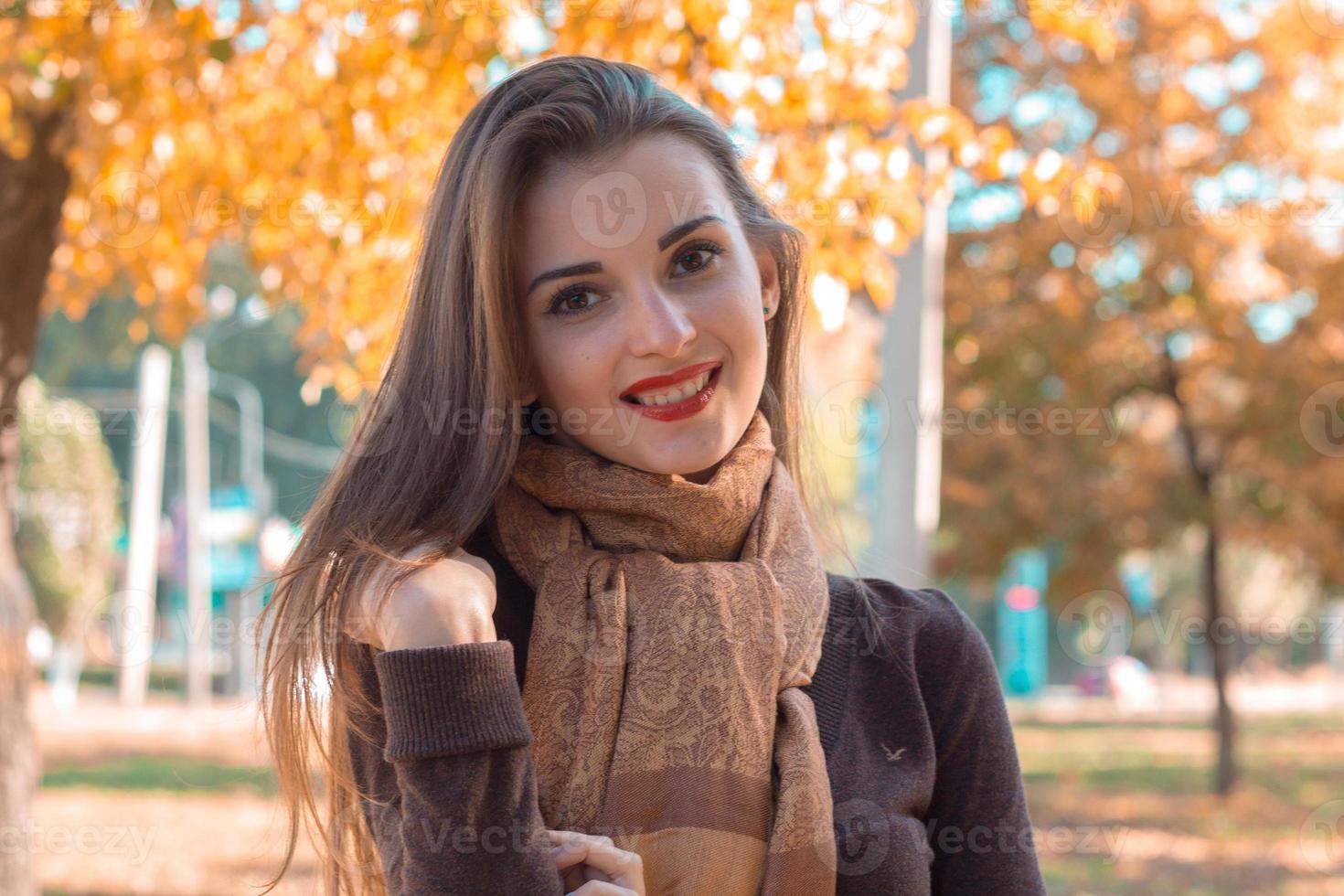 belle fille avec du rouge à lèvres et une écharpe brune se tient dans le parc sourit photo