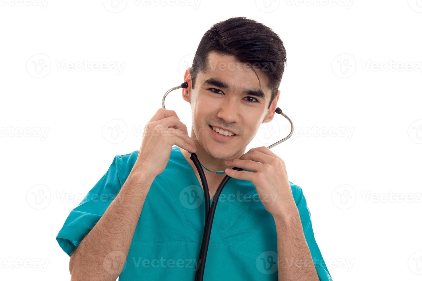 portrait de joyeux jeune homme brune médecin en uniforme bleu avec stéthoscope posant isolé sur fond blanc photo