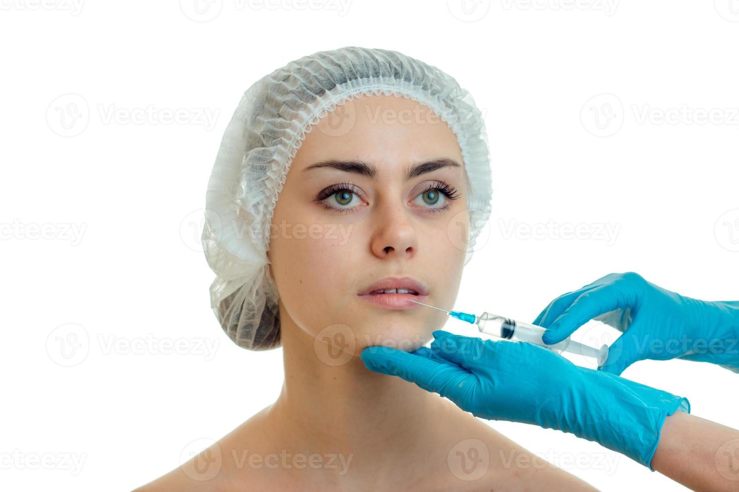 portrait d'une jeune fille dans une casquette médicale que le médecin injecte le vaccin sur le visage avec des mains gantées photo