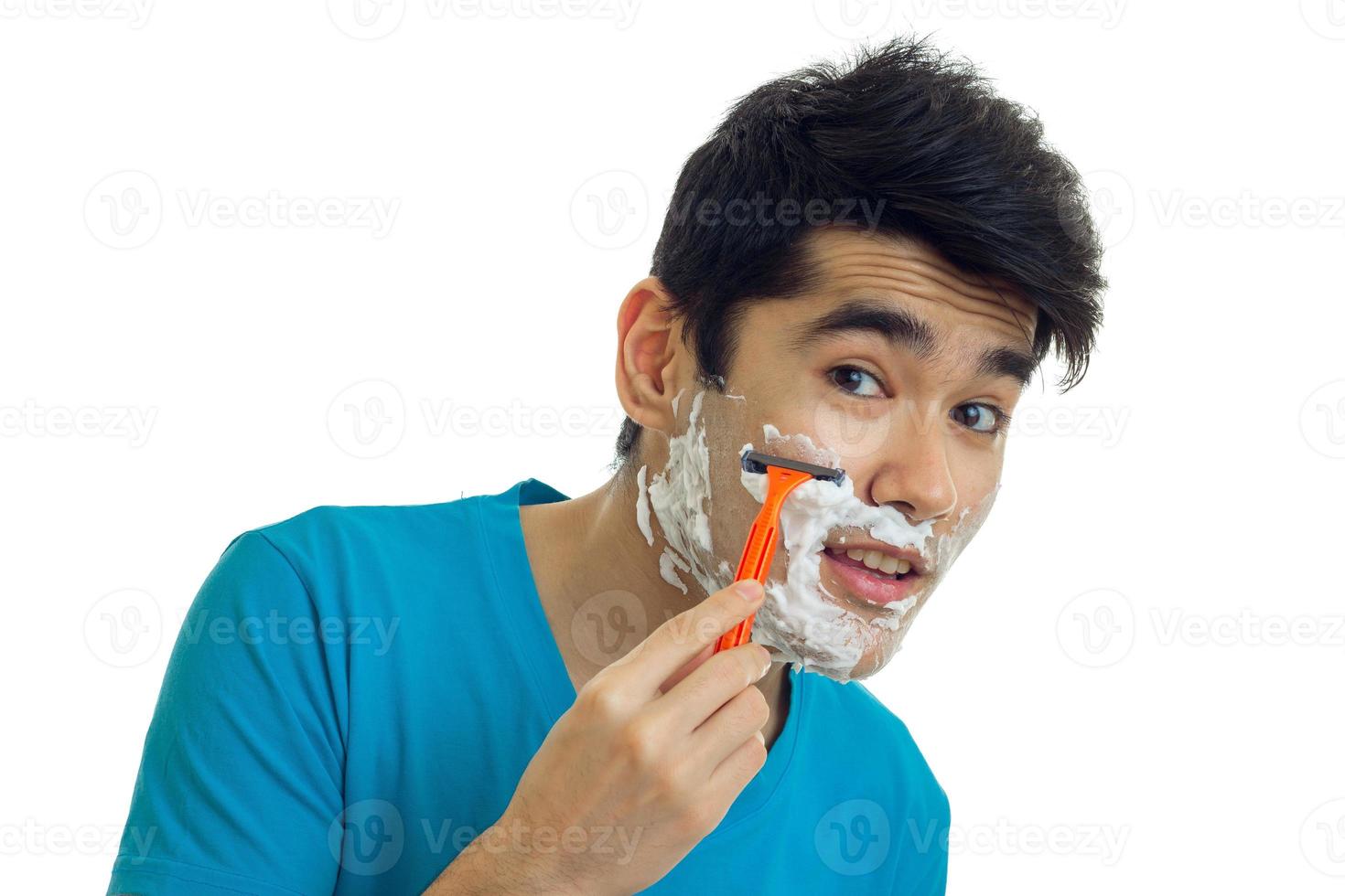 beau jeune homme aux cheveux noirs vaut la peine d'ouvrir la bouche regarde la caméra et se rase la barbe en gros plan photo