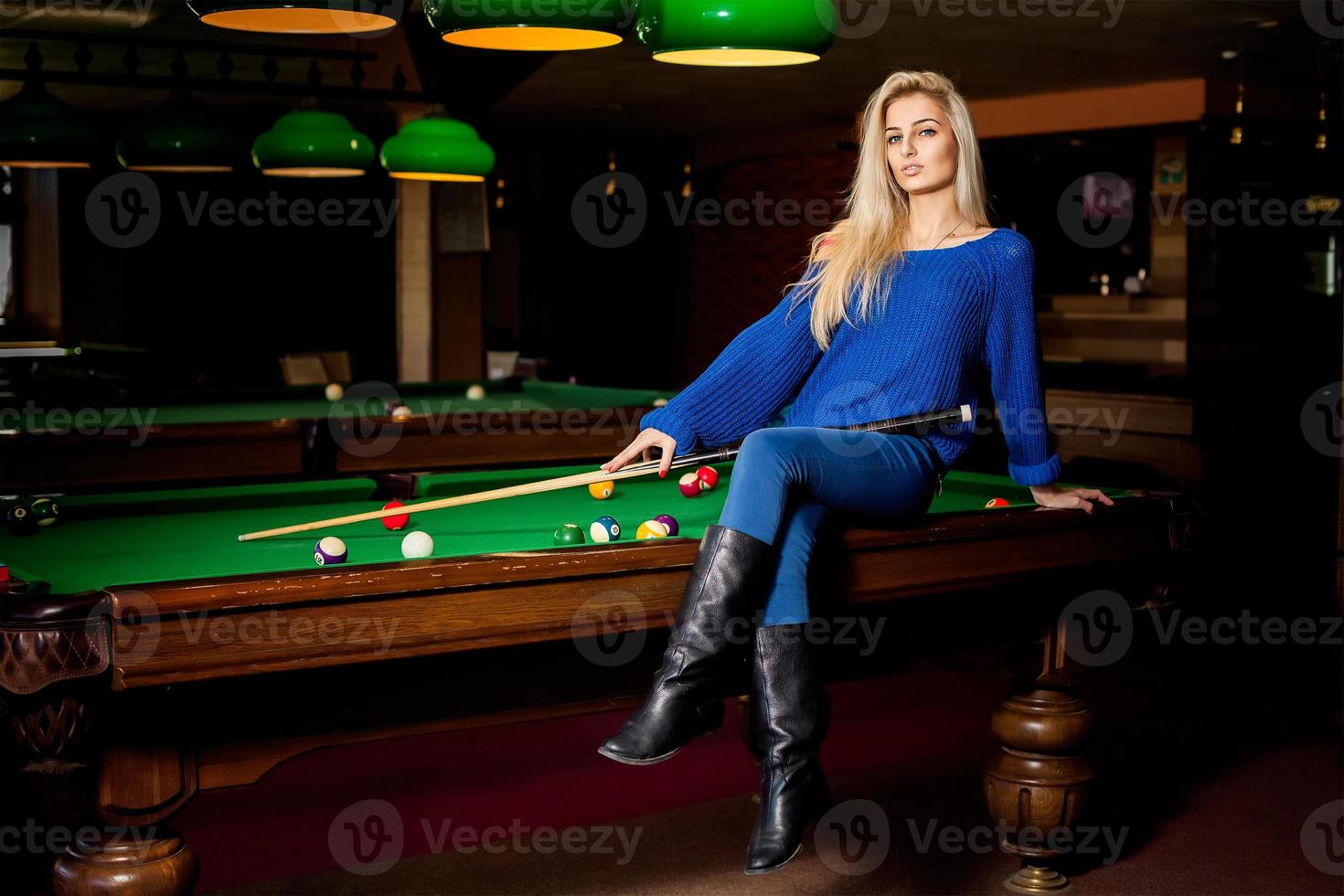 adorable femme de mode blonde posant sur une table de billard avec la queue photo