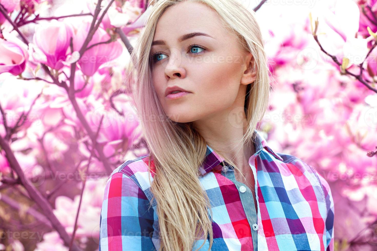 jolie jeune fille blonde regardant loin avec des fleurs roses derrière photo