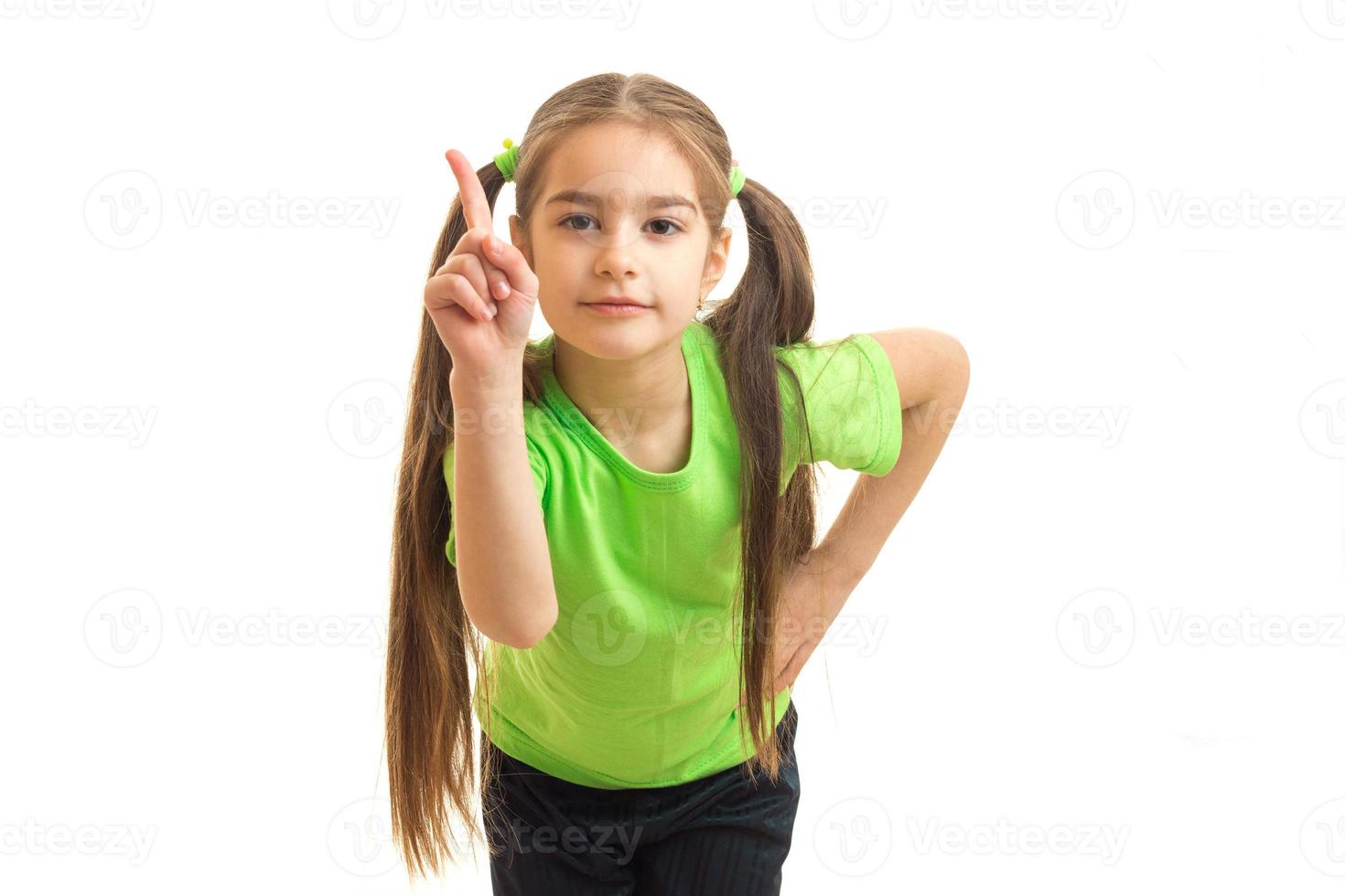 petite fille avec des queues et un t-shirt brillant posant en studio et montre le doigt photo