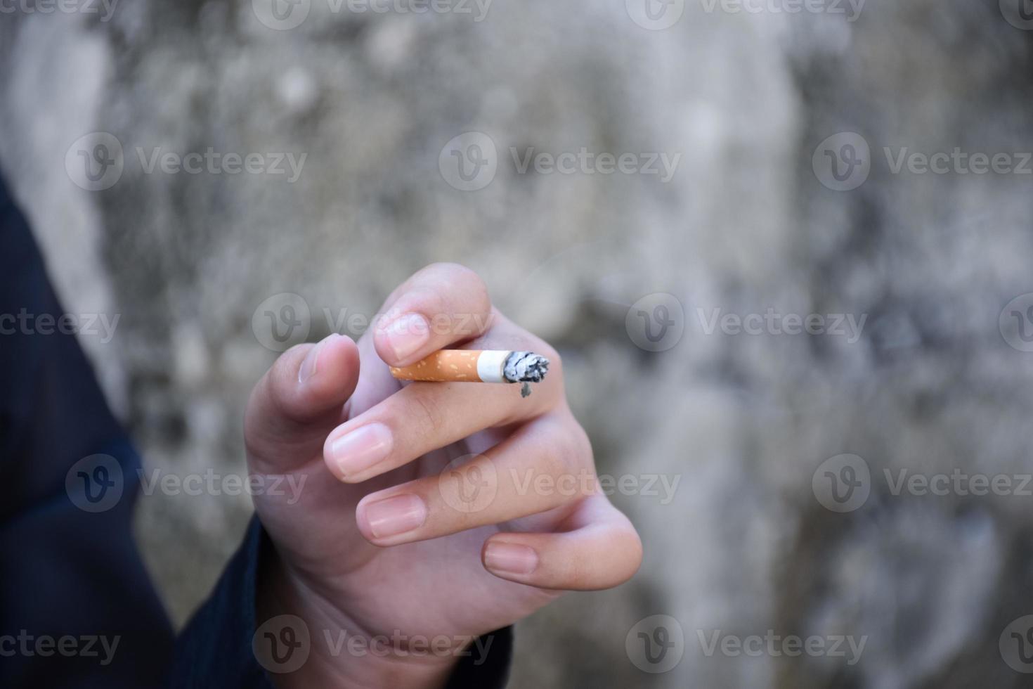 garçon apprenant à fumer par lui-même dans la zone située derrière la clôture de l'école qui est un endroit caché pour les gens, mauvaise influence de la vie au lycée ou au collège, dépendance. photo