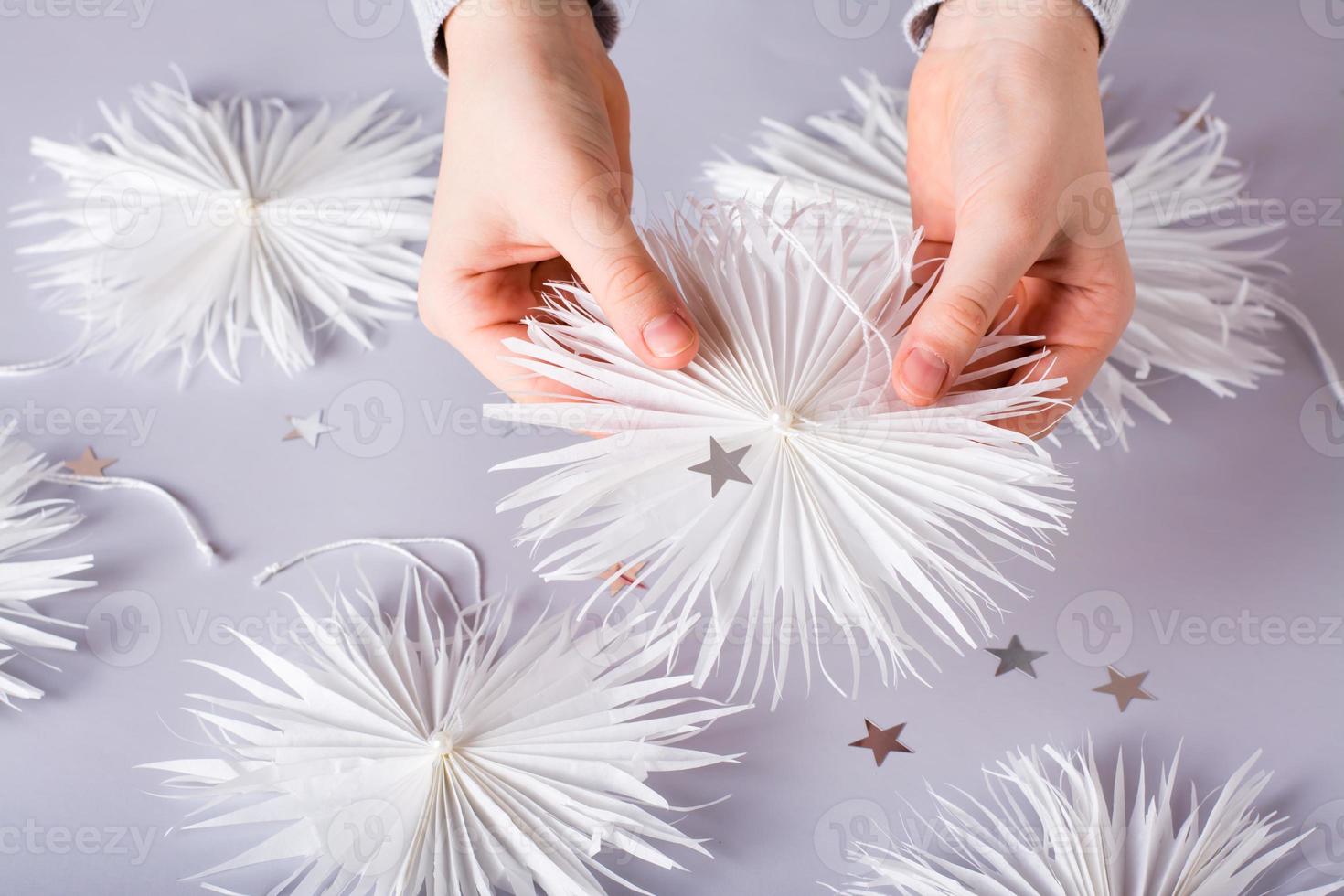 flocons de neige en papier de noël simples avec un fil et une perle dans les mains des enfants. décor fait à la main photo