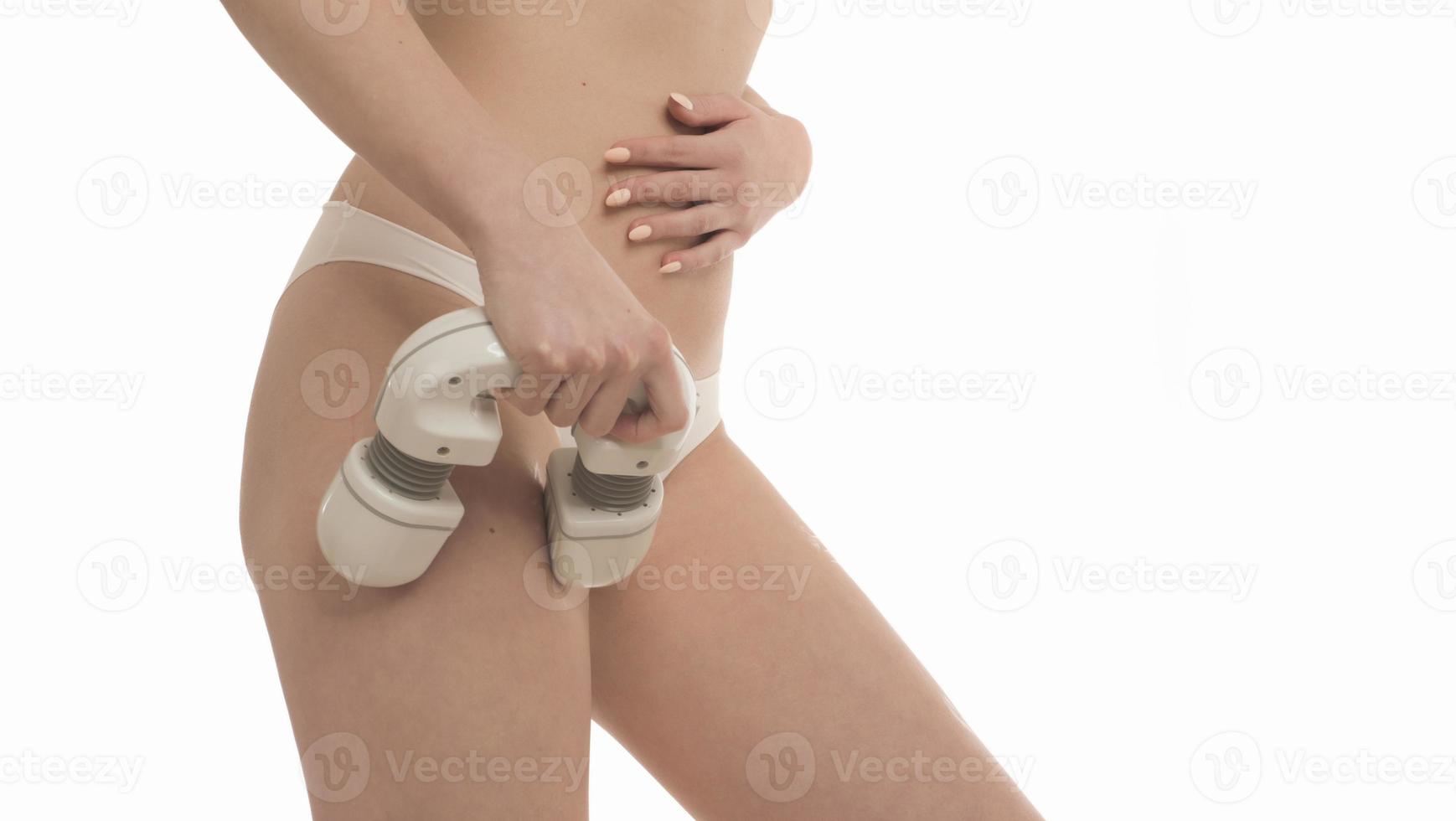 femme inconnue avec un corps en forme parfaite portant des sous-vêtements blancs massant ses hanches avec un masseur électrique. isolé sur fond blanc photo