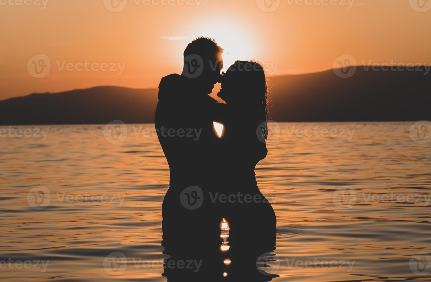 silhouettes amoureuses amoureux de couples romantiques étreignant, embrassant, touchant, contact visuel au coucher du soleil, lever de soleil sur le fond de la mer, le soleil, les nuages en rouge ardent, couleurs orange photo