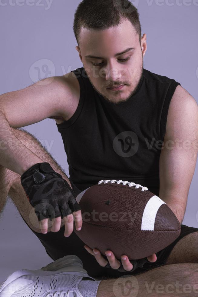 jeune bel homme américain tenant un ballon de rugby sur fond gris isolé photo