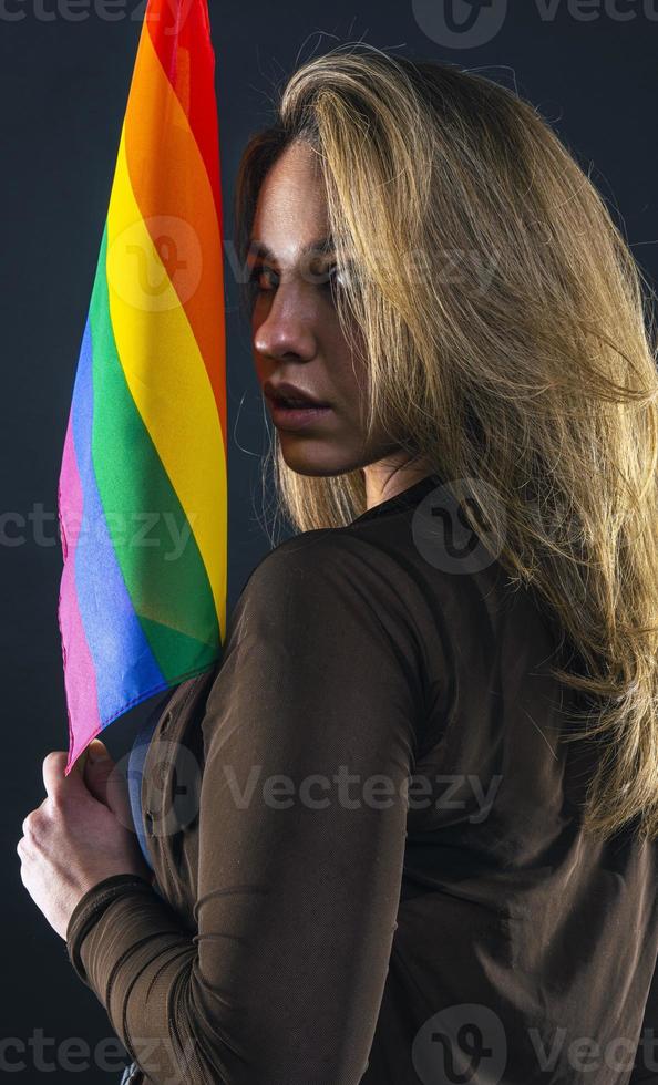 femme lesbienne tenant le drapeau arc-en-ciel isolé sur fond noir. symbole international lgbt de la communauté lesbienne, gay, bisexuelle et transgenre. photo