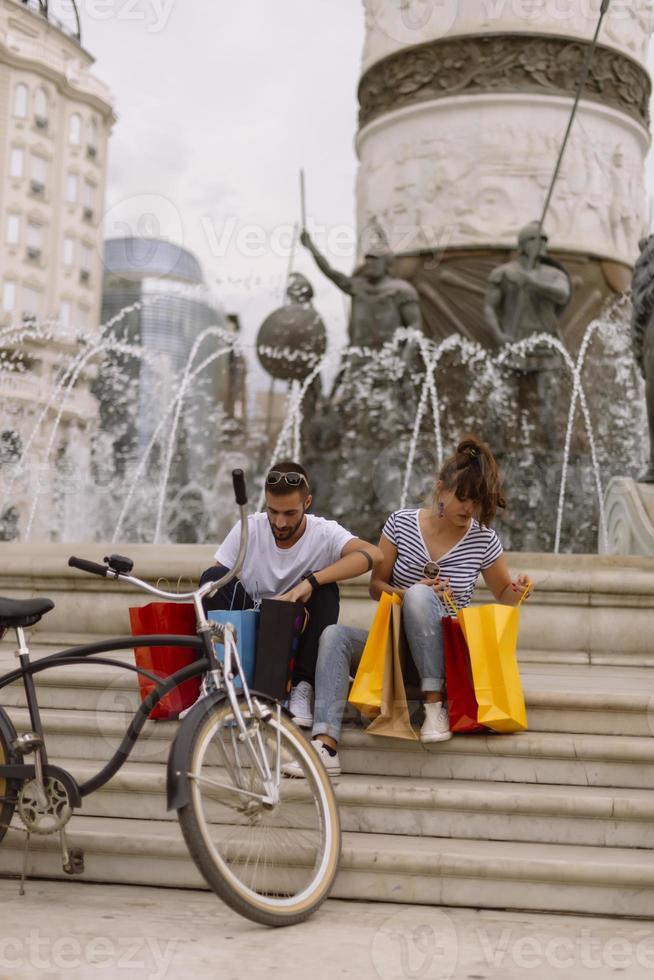 portrait d'un jeune couple caucasien joyeux homme et femme tenant de nombreux sacs en papier après avoir fait du shopping en marchant et en parlant dans la rue. couple de famille heureux avec forfaits en plein air. notion d'achat photo