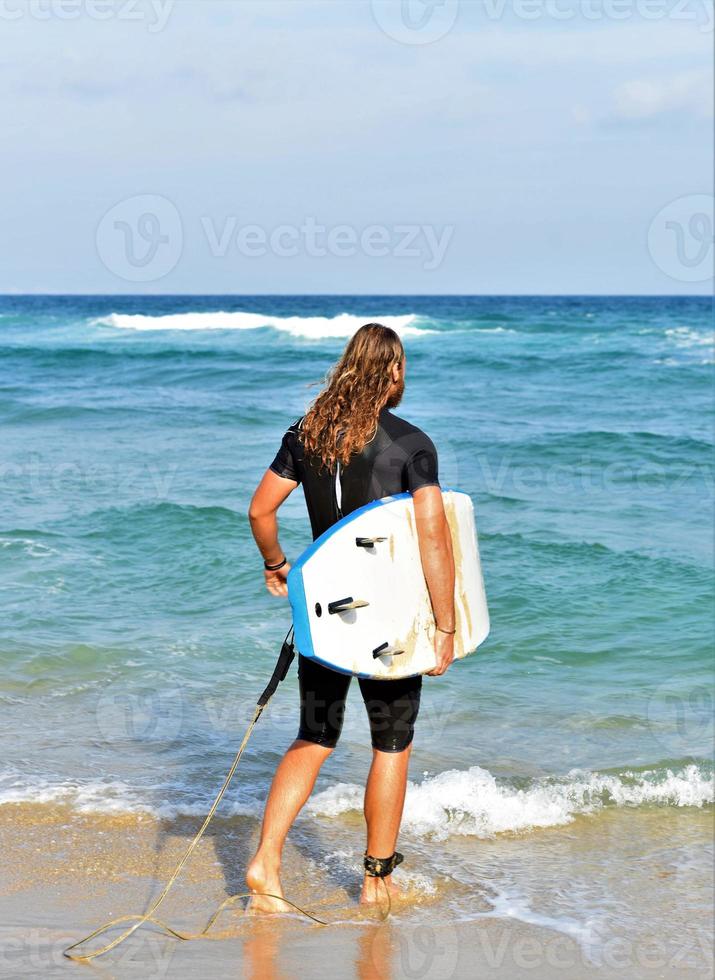 un homme est debout avec un surf dans ses mains sur le bord de la mer. photo