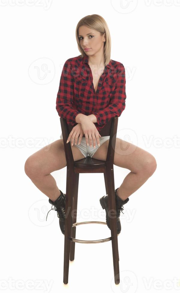 souriante jeune femme assise sur un tabouret. portrait en studio isolé sur le dos blanc. photo