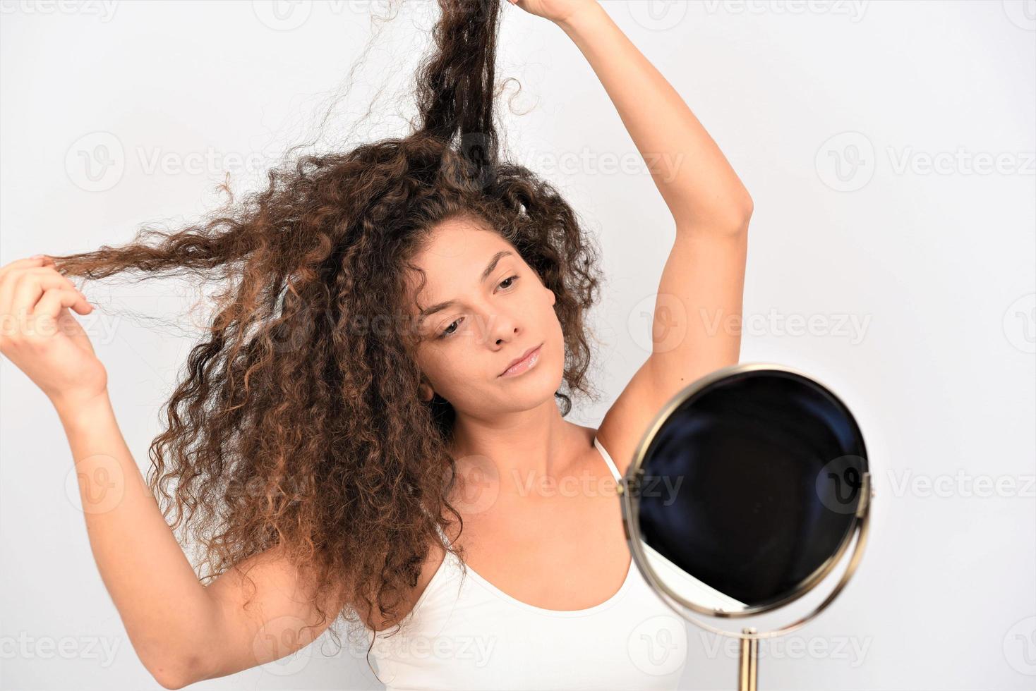 modèle féminin positif souriant pour la caméra et touchant des cheveux bouclés propres après une routine hygiénique photo
