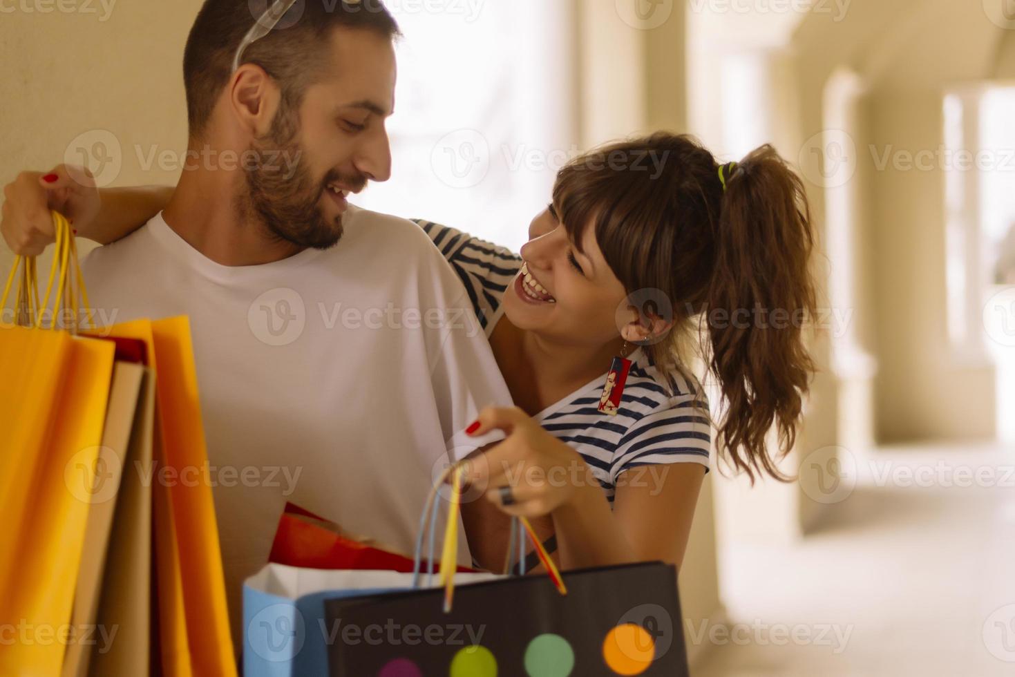 portrait d'un jeune couple caucasien joyeux homme et femme tenant de nombreux sacs en papier après avoir fait du shopping en marchant et en parlant dans la rue. couple de famille heureux avec forfaits en plein air. notion d'achat photo