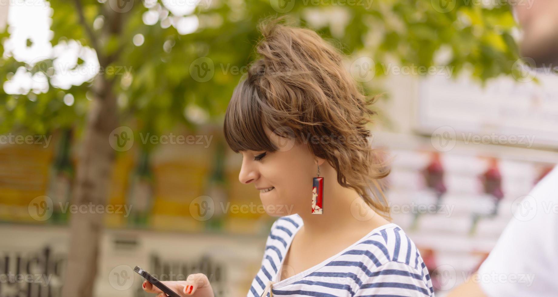 fille textos sur le téléphone intelligent dans une terrasse de restaurant avec un arrière-plan flou photo