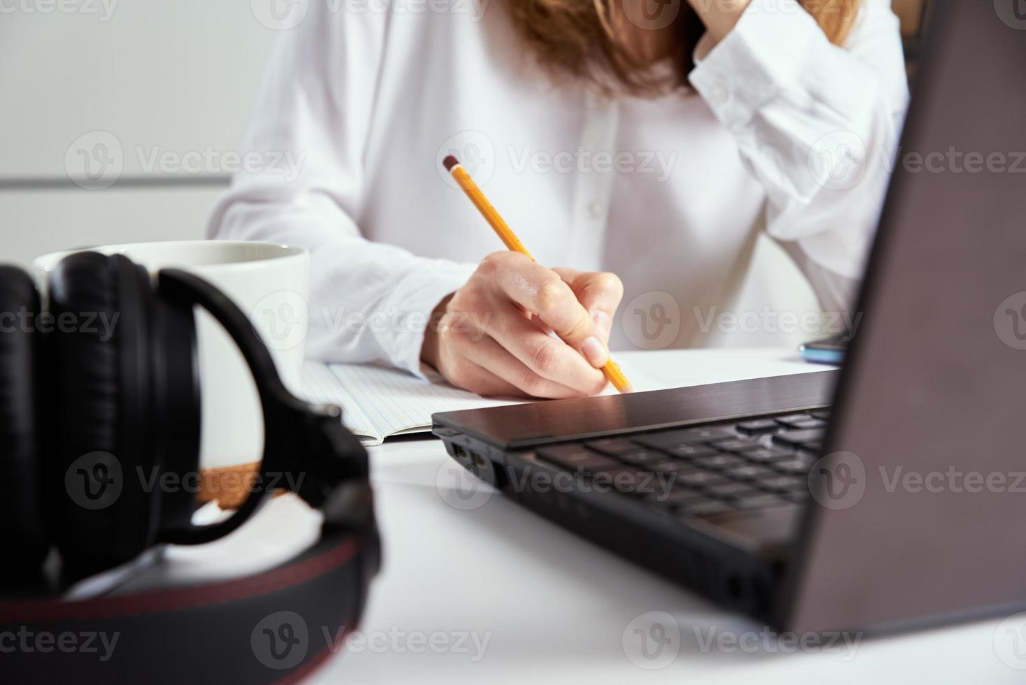 travail à distance. la femme prend des notes dans un cahier et utilise un ordinateur portable pour étudier. photo