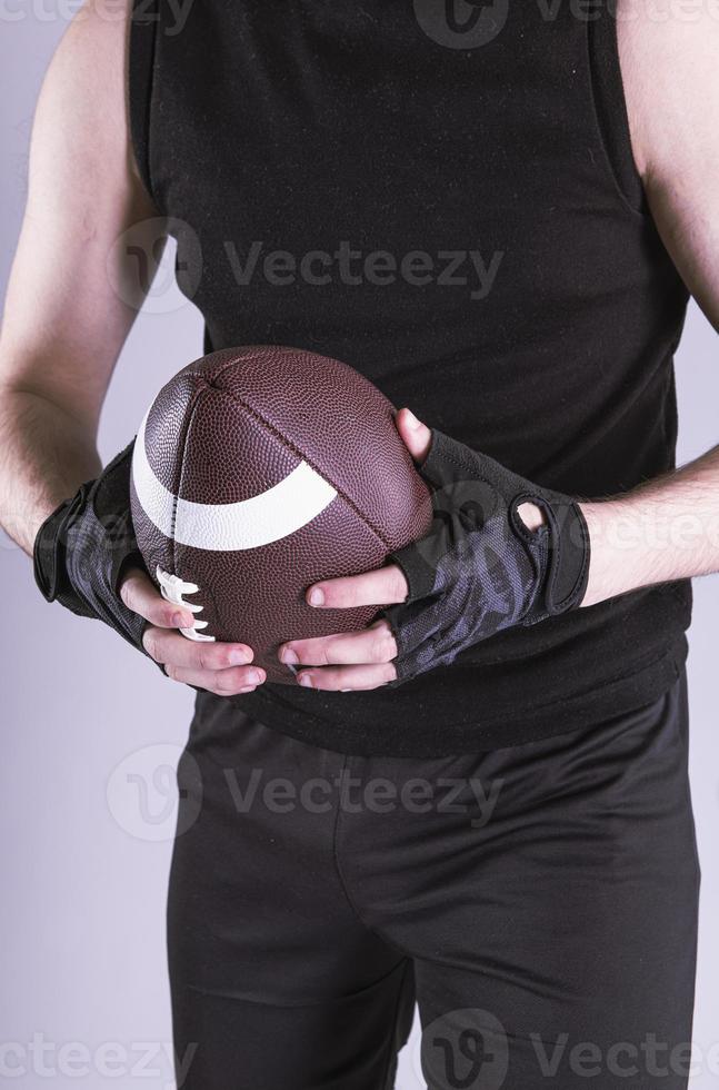 jeune bel homme américain tenant un ballon de rugby sur fond gris isolé photo