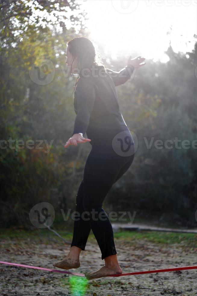 femme équilibrant sa marche sur une corde lâche attachée entre deux arbres. femme pratiquant le mou de la corde marchant dans un parc. photo