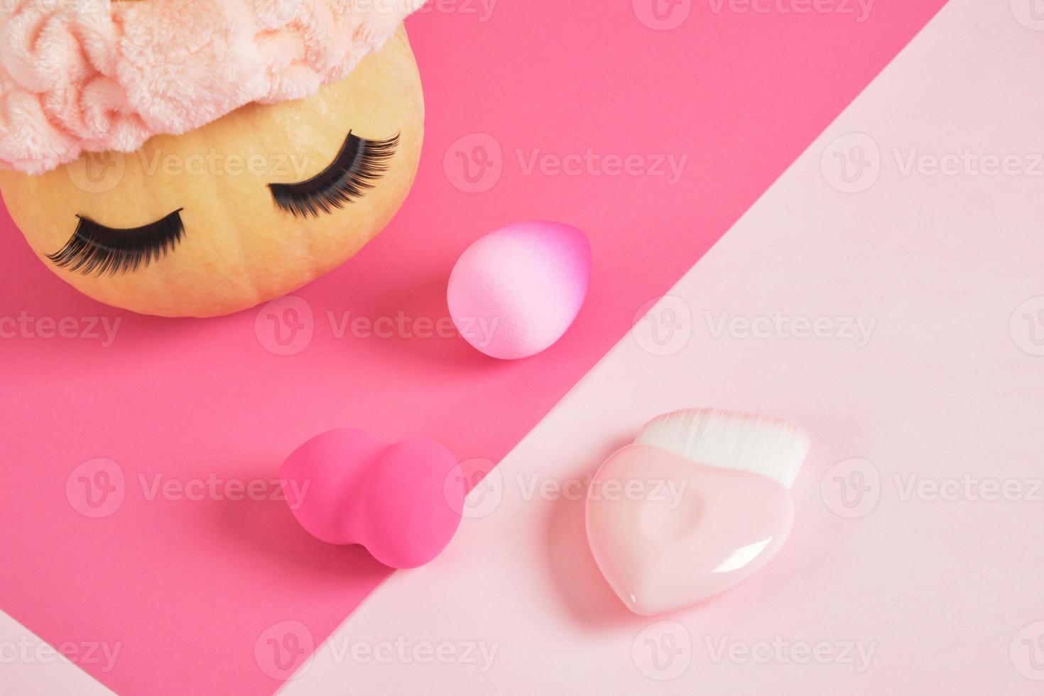 citrouille dans un bandeau et faux cils sur fond rose, éponges pour appliquer le maquillage salon de beauté photo