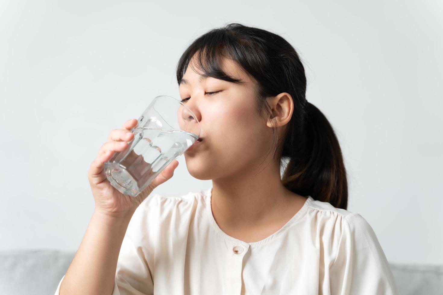 belle jeune femme en bonne santé tenant un verre d'eau potable assise sur le canapé du salon. photo