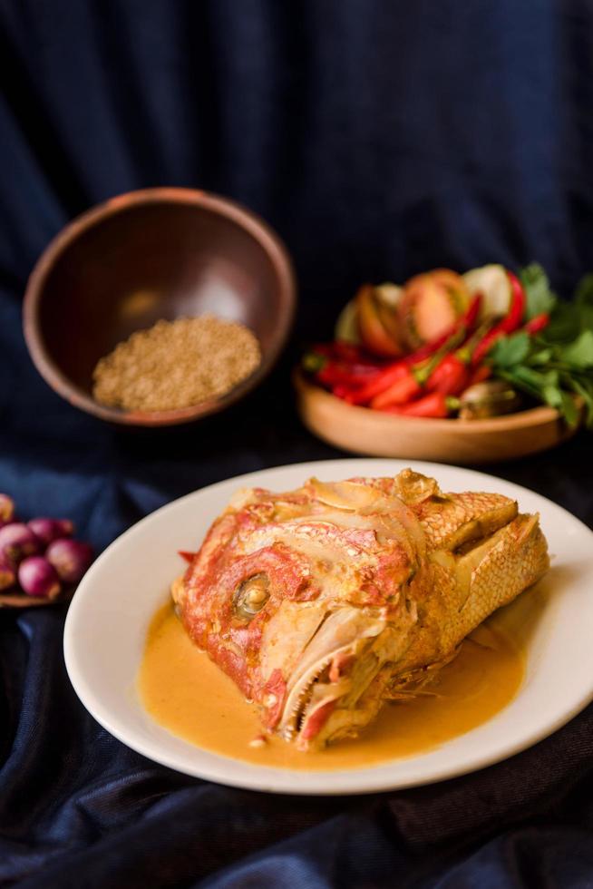 poisson frit dans une sauce curry épicée sur un plat blanc. nourriture indonésienne photo