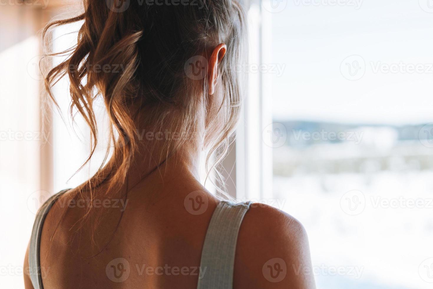 photo en gros plan d'une jeune femme blonde de remise en forme mince de dos près de la fenêtre de la maison