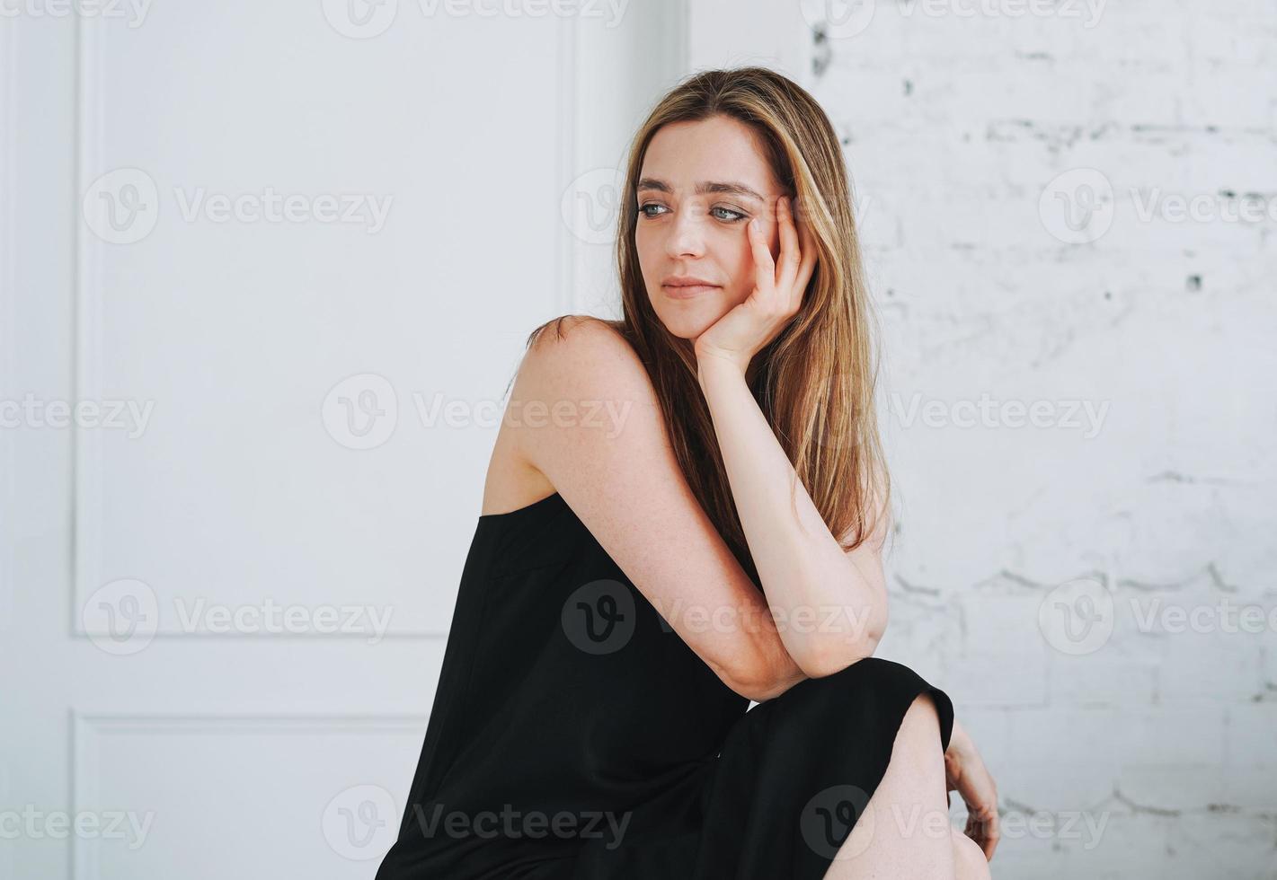 portrait de beauté de mode d'une jeune femme heureuse aux cheveux longs le soir élégante robe noire en intérieur blanc photo