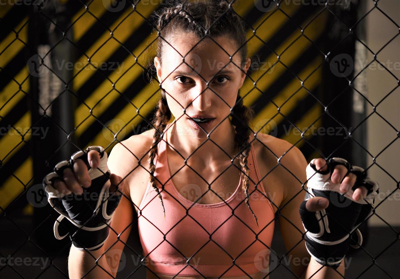 une stagiaire en arts martiaux mixtes portant un enveloppement à la main se réchauffe dans la cage de l'anneau en étirant son dos et ses jambes. photo