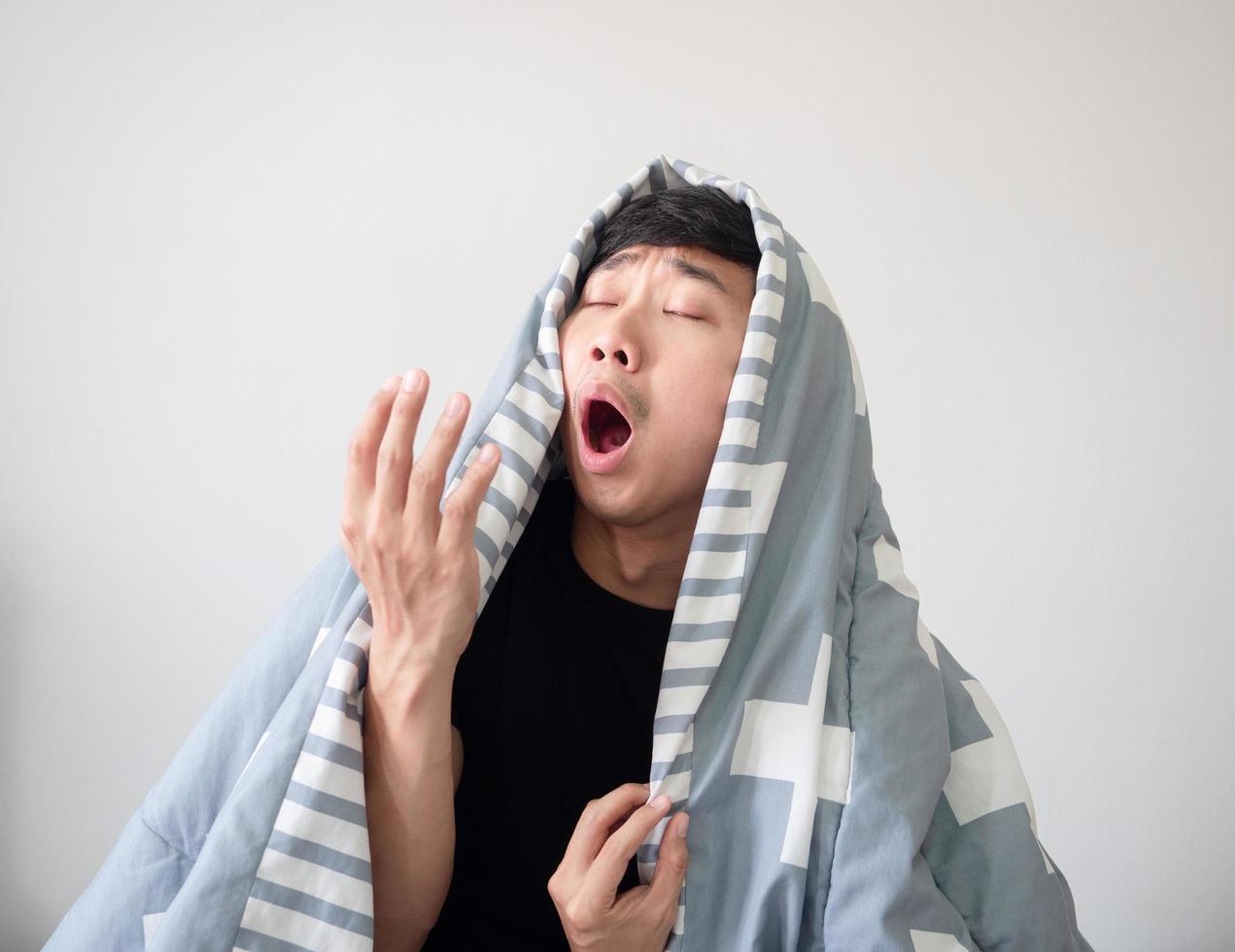 jeune homme avec couverture couvrir son corps se réveiller et se sentir somnolent et bâiller sur blanc isolé, concept d'homme endormi photo