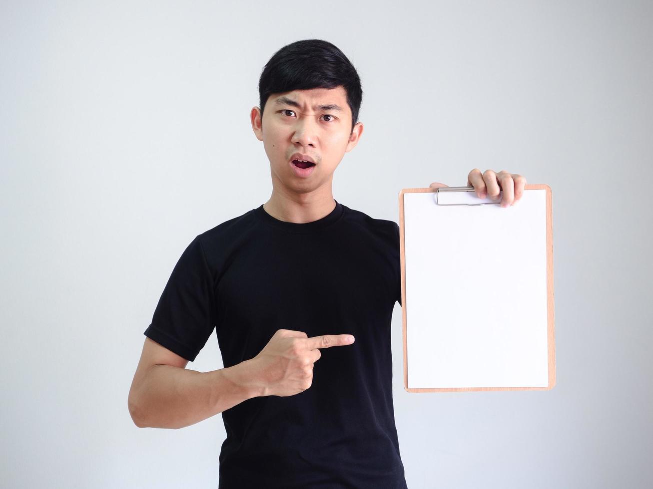 jeune homme asiatique chemise noire pointer du doigt le presse-papiers en bois document vierge dans la main visage sérieux sur blanc isolé photo