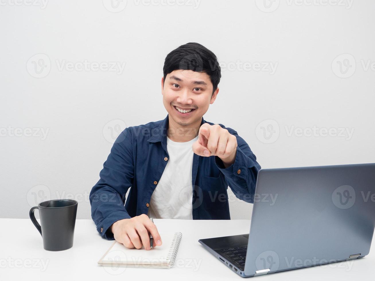 homme souriant avec lieu de travail sur le bureau et pointant du doigt vers vous une émotion souriante photo