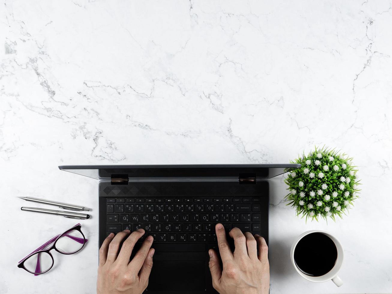 Main sur ordinateur portable clavier avec verres stylo argent tasse à café vase à fleurs sur table en marbre concept de travail espace copie vue de dessus photo