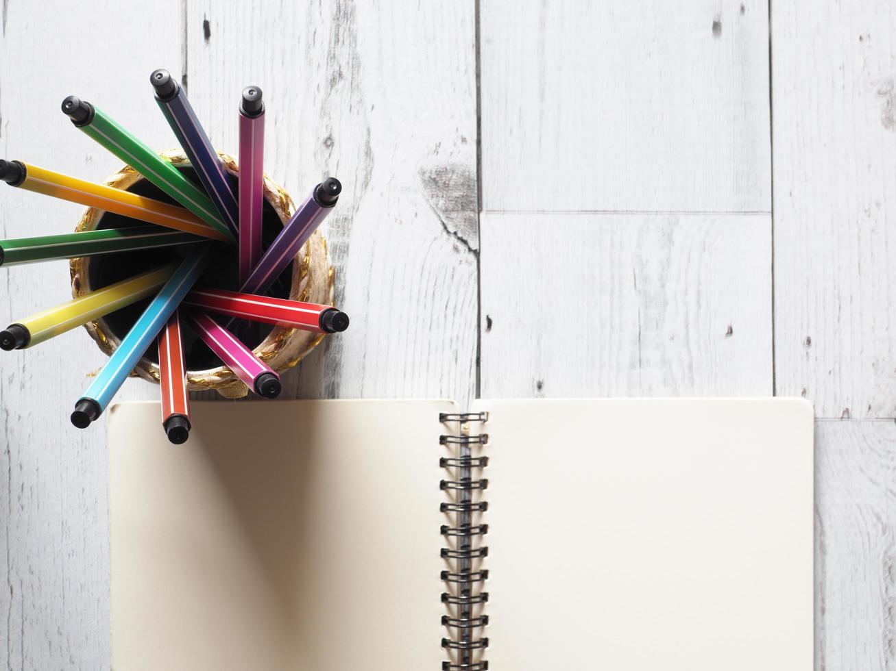 beaucoup de cercle de tableau coloré de stylo dans une boîte avec une page vierge de cahier ouvert sur une table en bois blanc et la lumière de la nature du concept d'idée de soleil vue de dessus, affaires et éducation photo