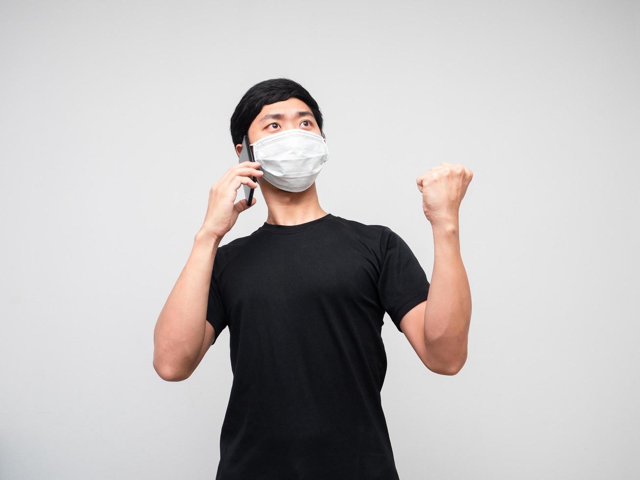un homme portant un masque de protection reçoit de bonnes nouvelles avec monie téléphone et montre le poing vers le haut sur fond blanc photo