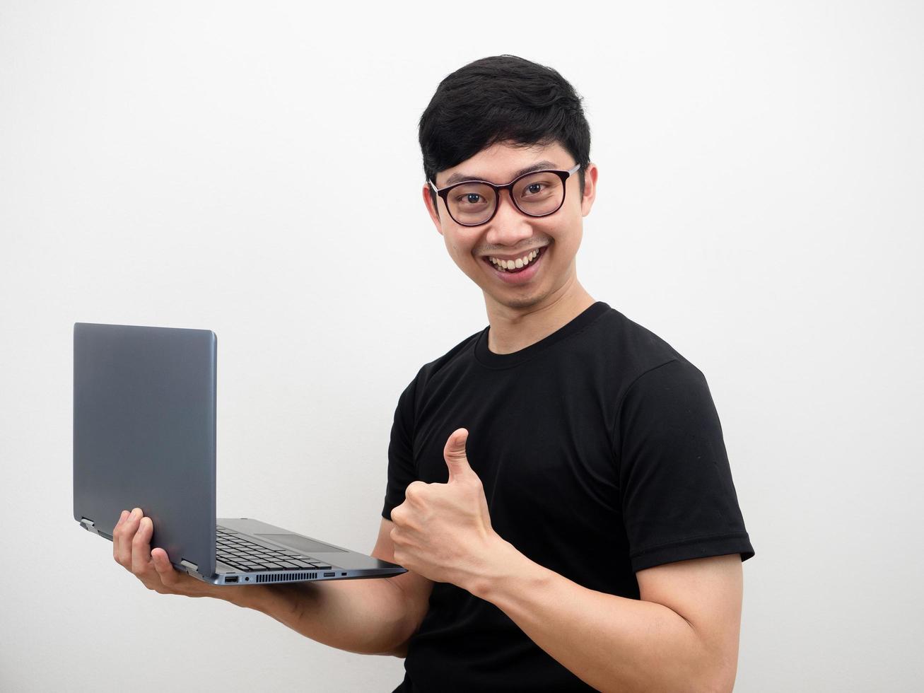 homme asiatique portant des lunettes visage confiant tenant un ordinateur portable montrer le pouce vers le haut sourire heureux sur fond blanc photo