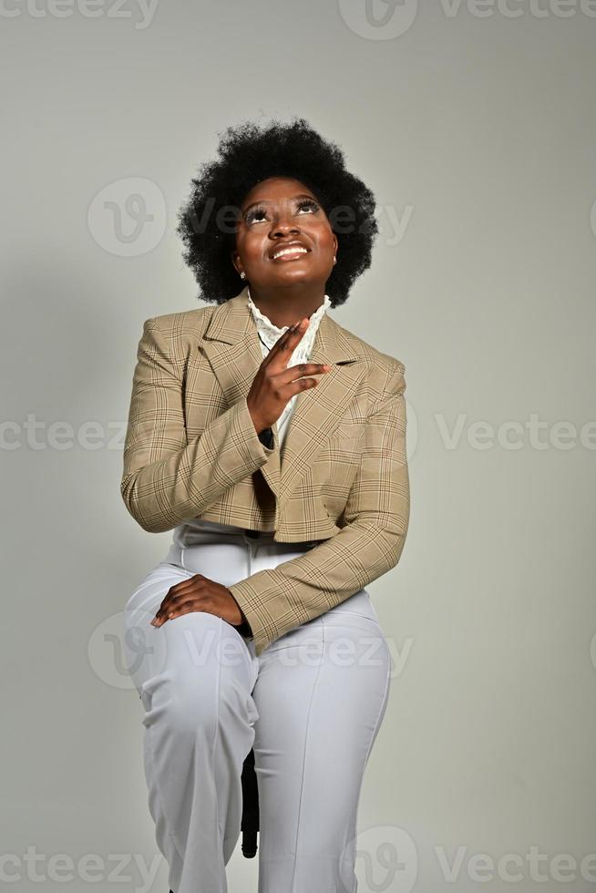 jolie femme afro-américaine avec des accessoires à la mode et une coiffure afro regardant la caméra sur fond gris photo