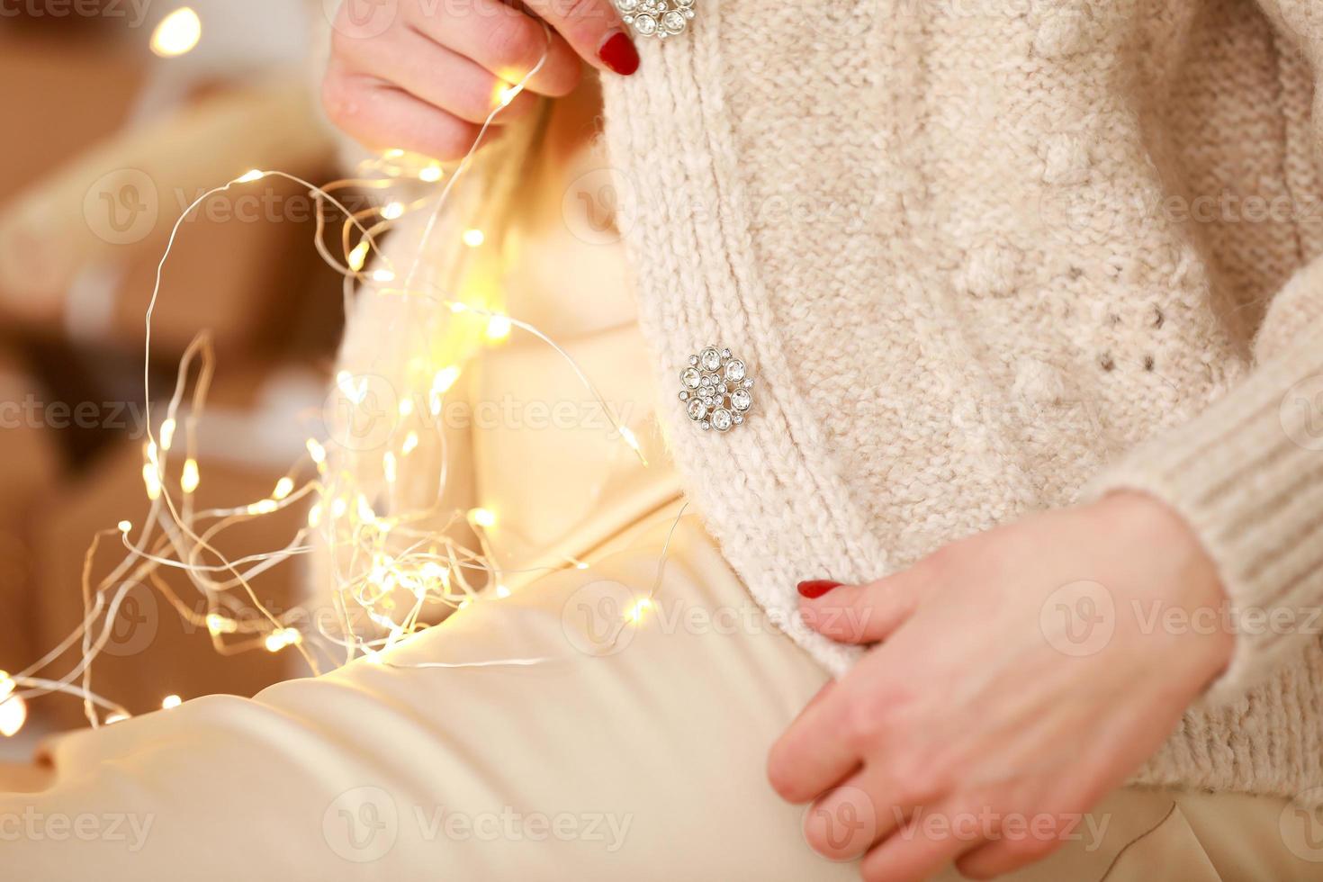 photo recadrée d'un élégant tissu tricoté luxueux et de détails de boutons de jeune femme avec une lumière de guirlande sur fond de décorations de noël.